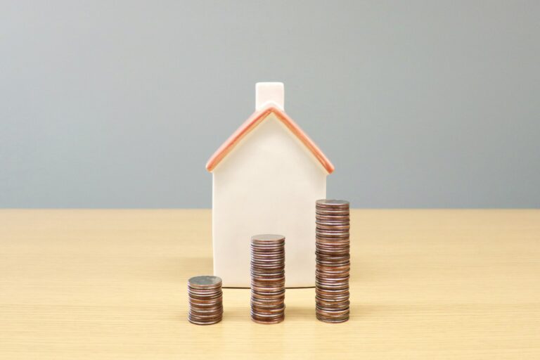 Grundsteuer: Hausmodell und Münzstapel als Symbol für die Steuer auf Wohneigentum