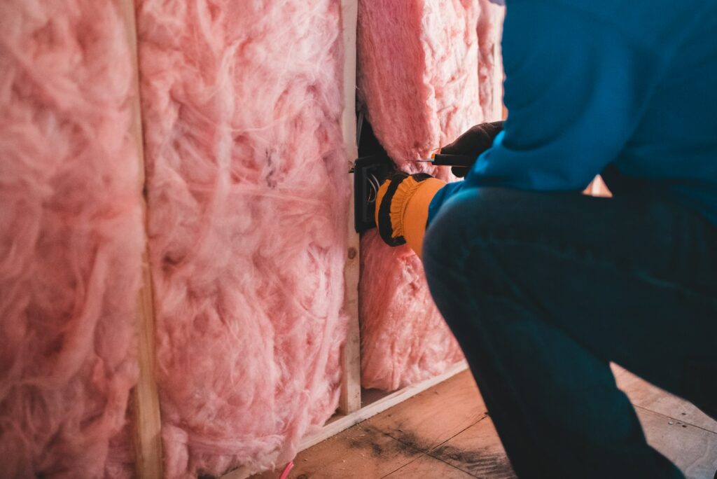 Dach dämmen: Mineralwolle zwischen Holzständern, ein Handwerker verlegt Leitungen