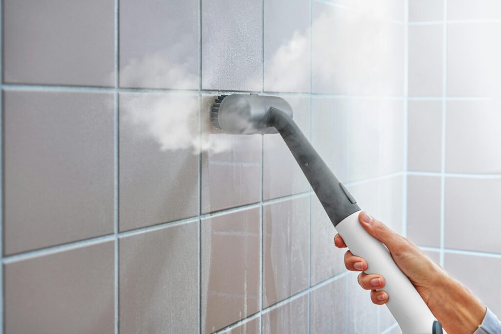 Dampfreiniger reinigt eine geflieste Wand im Badezimmer – Fugen gegen Schimmel pflegen