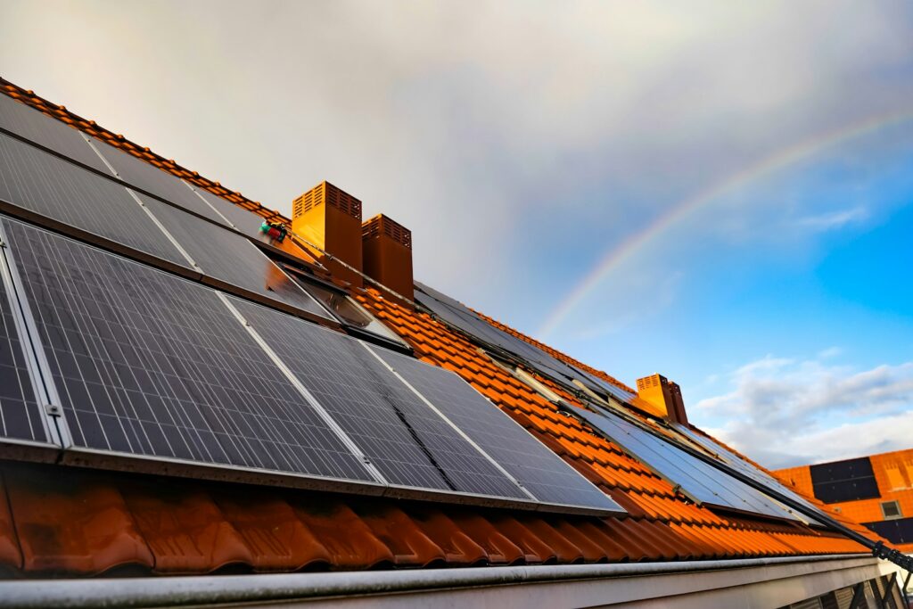 Förderung Sanierung: Solarmodul auf einem Dach vor einem Regenbogen