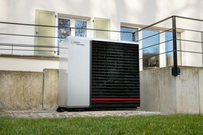 Gasheizung auf Wärmepumpe umrüsten: weiße Außeneinheit einer Wärmepumpe vor einem Wohnhaus