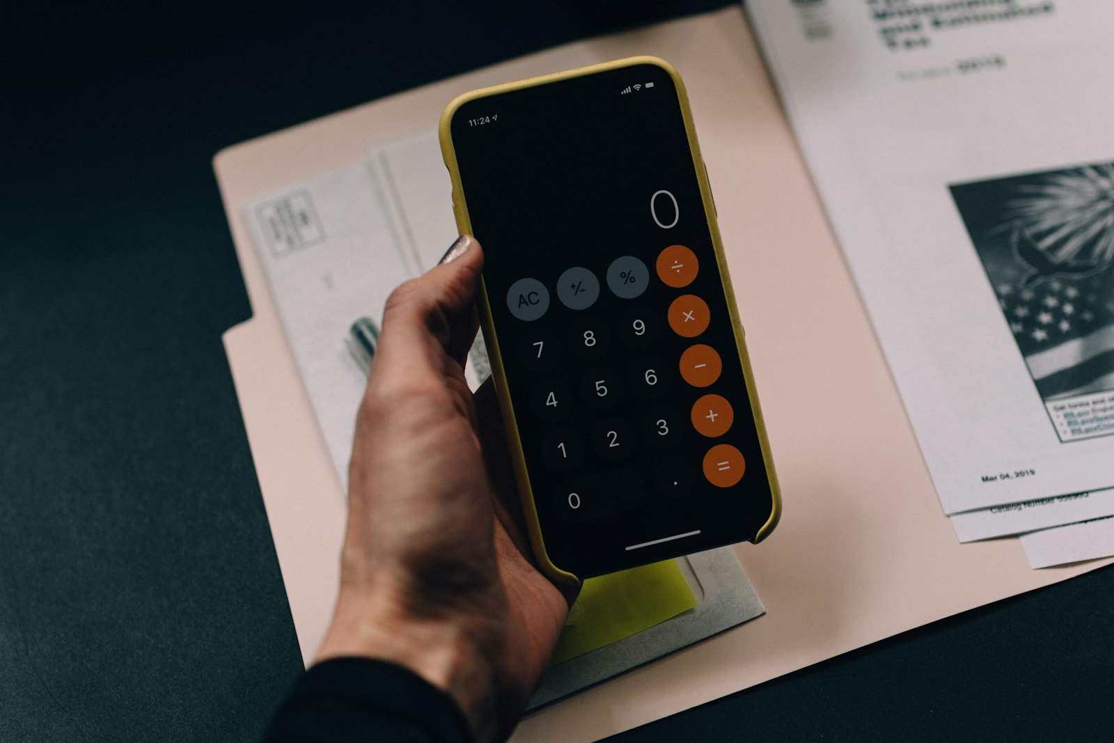 Grundsteuer verfassungswidrig: Hand hält Smartphone mit Taschenrechner über Steuerunterlagen