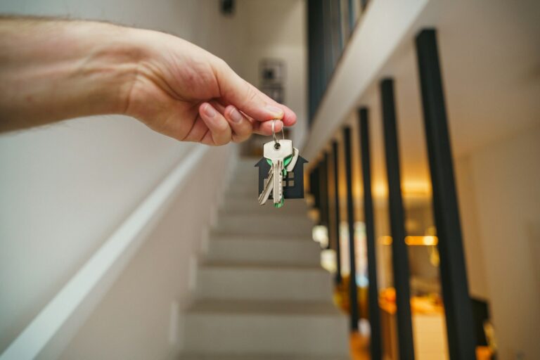 Haus geerbt: Hand hält Schlüssel mit Haus-Anhänger vor einer Treppe