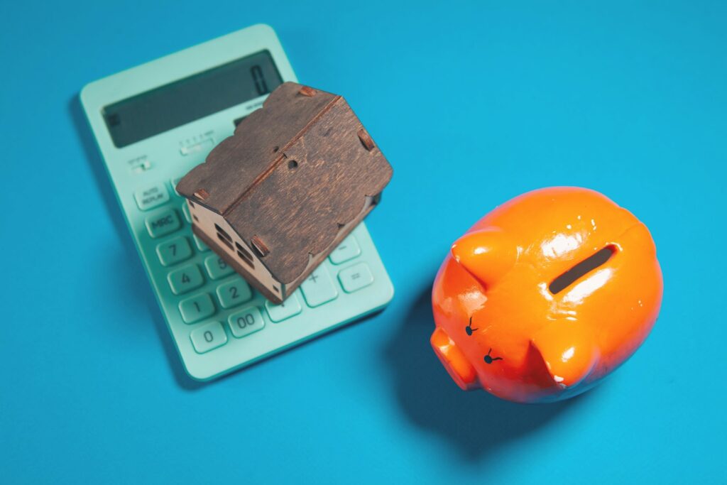 Hauskauf ohne Eigenkapital: Hausmodell, Sparschwein und Taschenrechner auf blauem Hintergrund