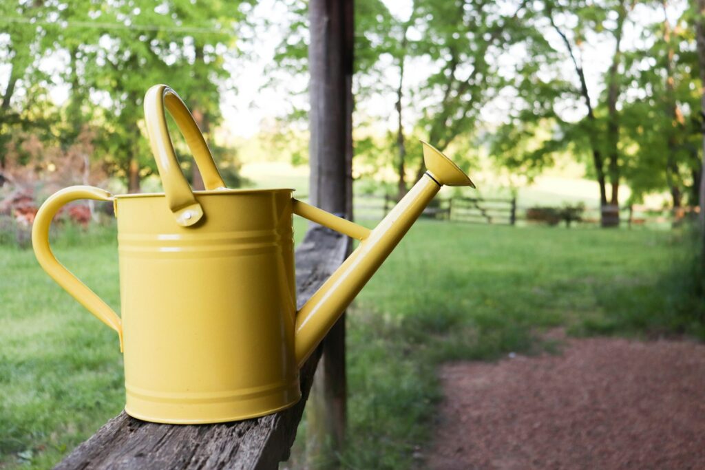 Regenwasser nutzen: gelbe Gießkanne auf einem Holzpfosten im Garten