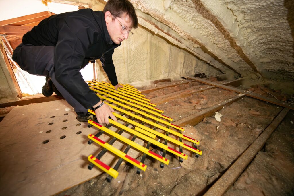 Sanierungspflicht erben: Handwerker verlegt eine Arbeitsmatte auf dem Dachboden