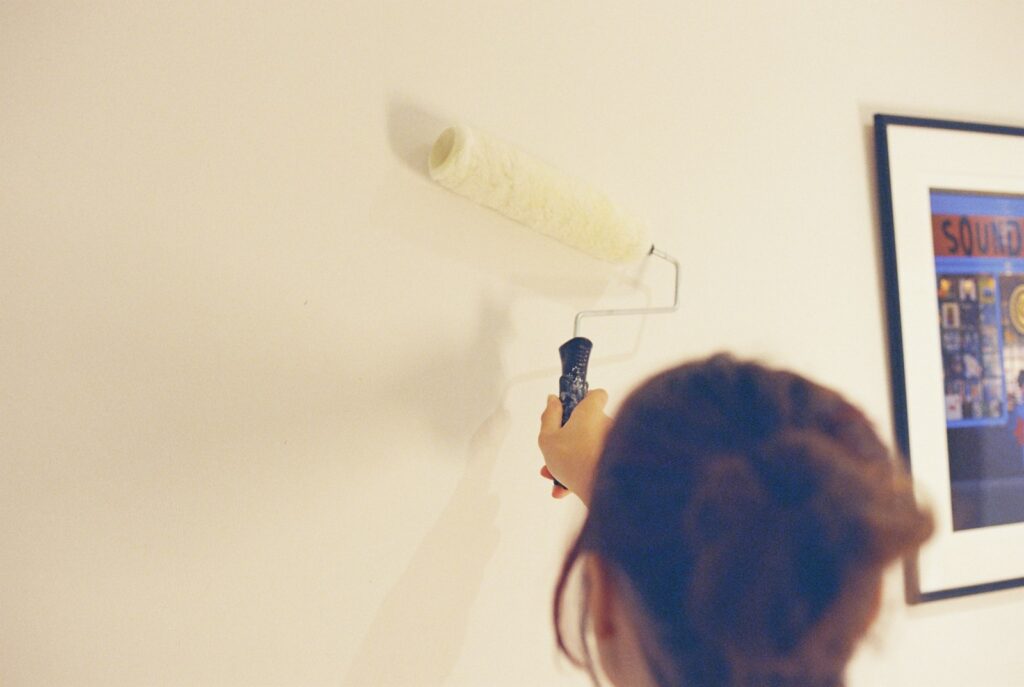 Wandfarben Wohnzimmer auftragen: Person streicht eine helle Wand mit der Farbrolle