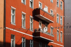 Wohngebäudeversicherung umlegen: rote Fassade eines Mehrfamilienhauses mit weißen Fenstern und Balkon