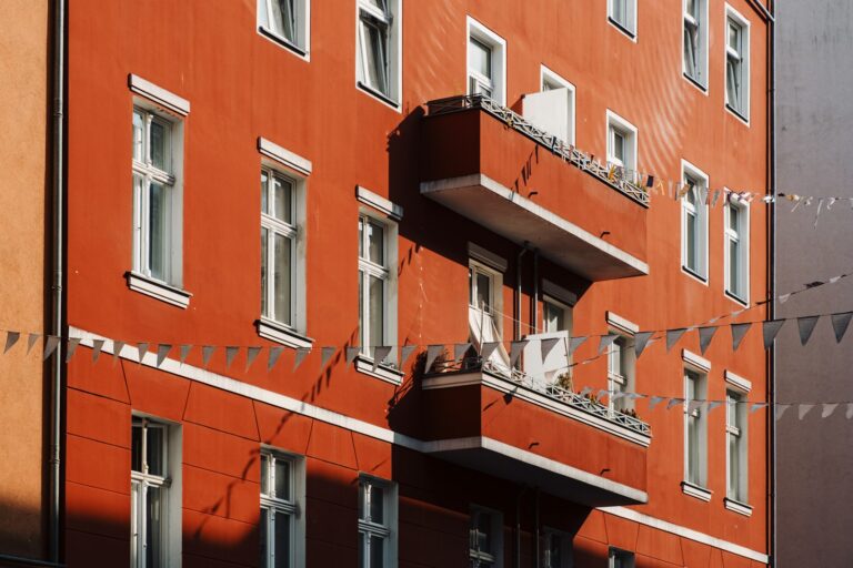 Wohngebäudeversicherung umlegen: rote Fassade eines Mehrfamilienhauses mit weißen Fenstern und Balkon